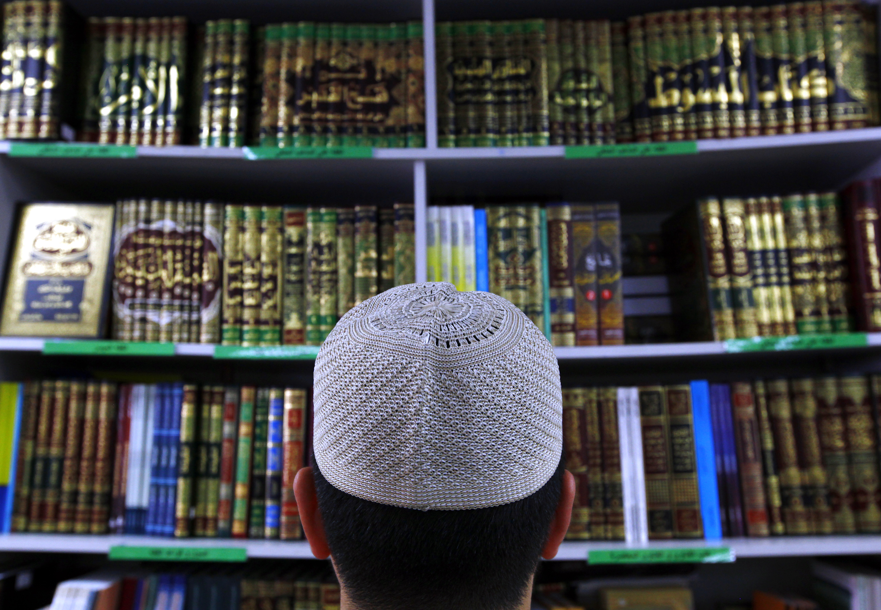 Man wearing an Islamic prayer cap, or “Kufi”, looks at Islamic books on